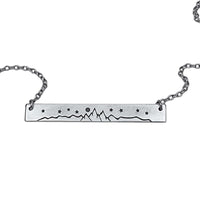 High Alpine Necklace featuring a brass mountain landscape design, adjustable chain, and available in matte silver and antique brass finishes.