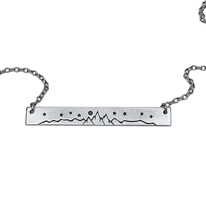 High Alpine Necklace featuring a brass mountain landscape design, adjustable chain, and available in matte silver and antique brass finishes.