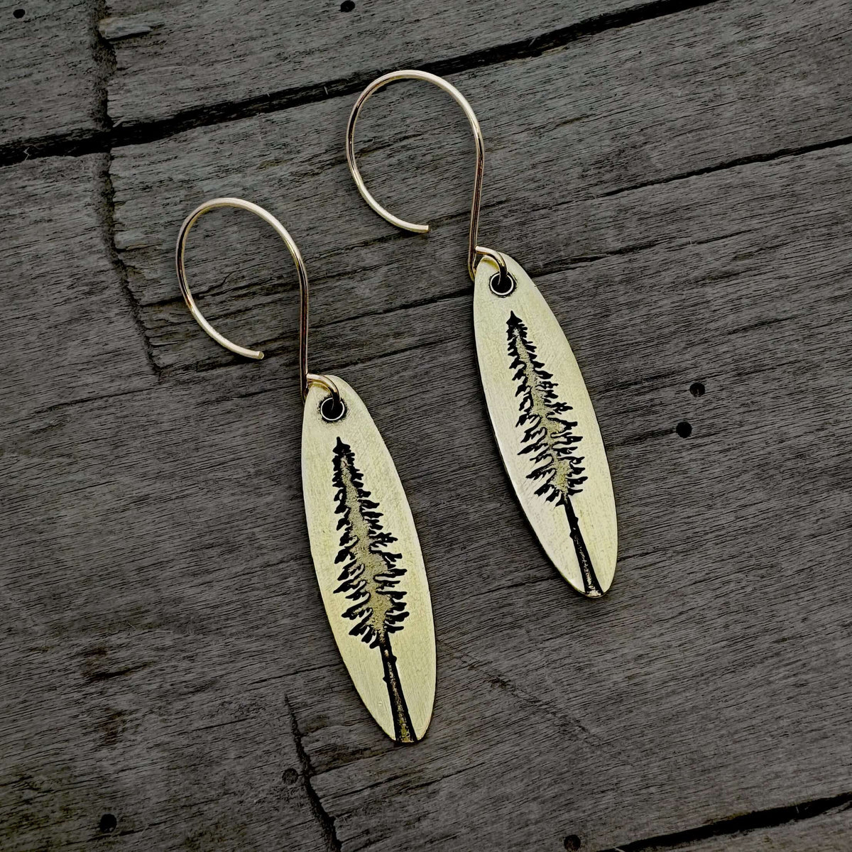 Larch Tree Earrings featuring an etched design of a larch tree on raw brass with a matte silver finish.