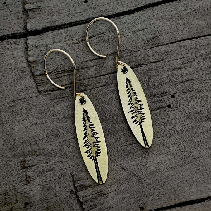 Larch Tree Earrings featuring an etched design of a larch tree on raw brass with a matte silver finish.