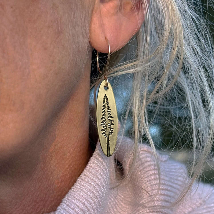 Larch Tree Earrings showcasing an etched larch tree design, worn by a woman with light hair.