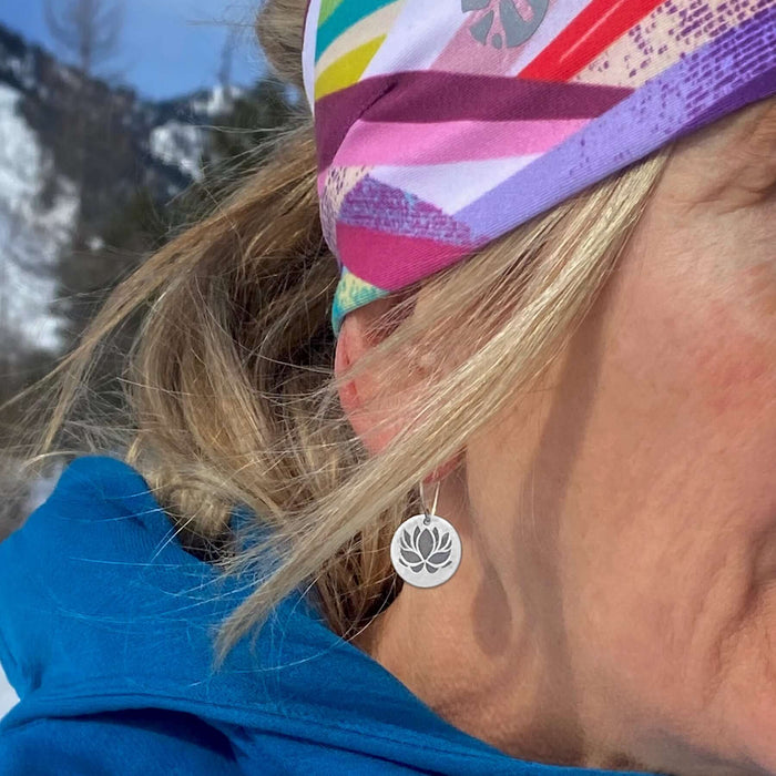 Close-up of model wearing Lotus Flower Earrings with a colorful headband against a mountainous backdrop.