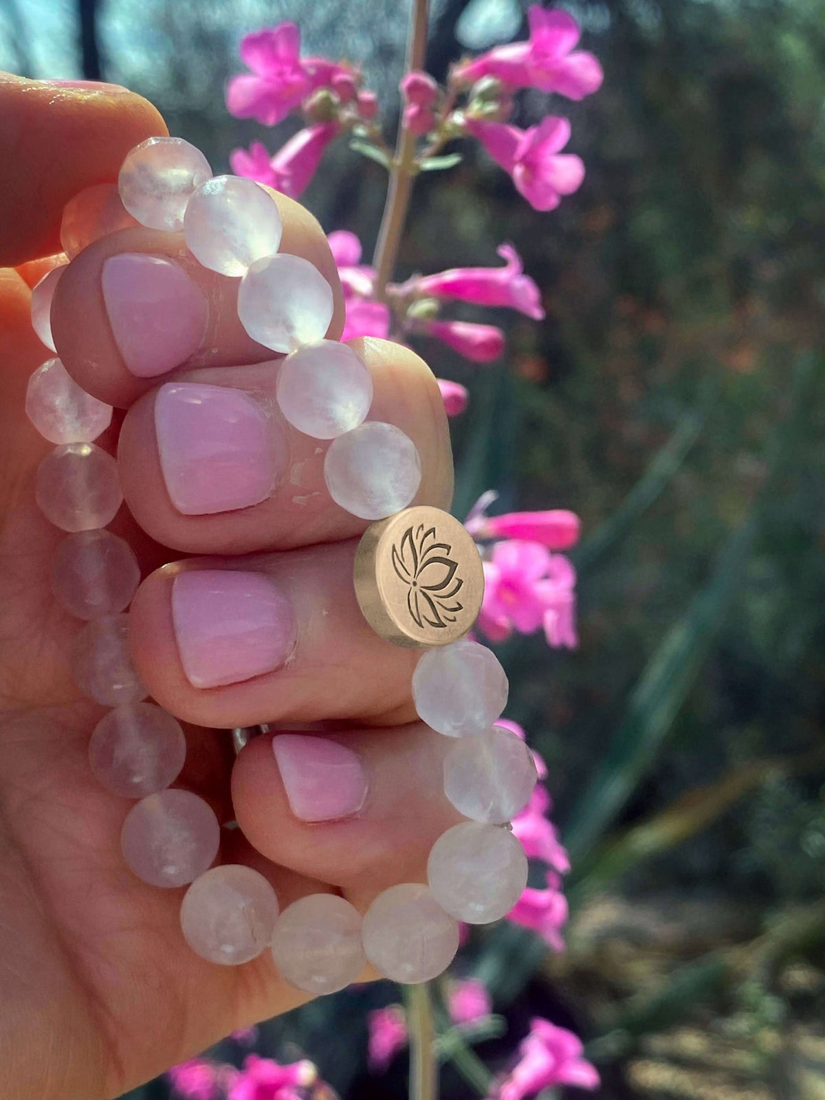 Lotus Stretch Bracelet - Gemstone Beaded Stretchy Bracelet held in hand with flowers in background.