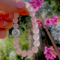 Lotus Stretch Bracelet - Gemstone Beaded Stretchy Bracelet with rose quartz beads and lotus charm, surrounded by flowers.