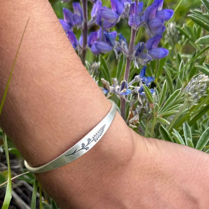 Lupine Flower Cuff Bracelet worn on wrist with lupine flowers in background, showcasing intricate floral design.