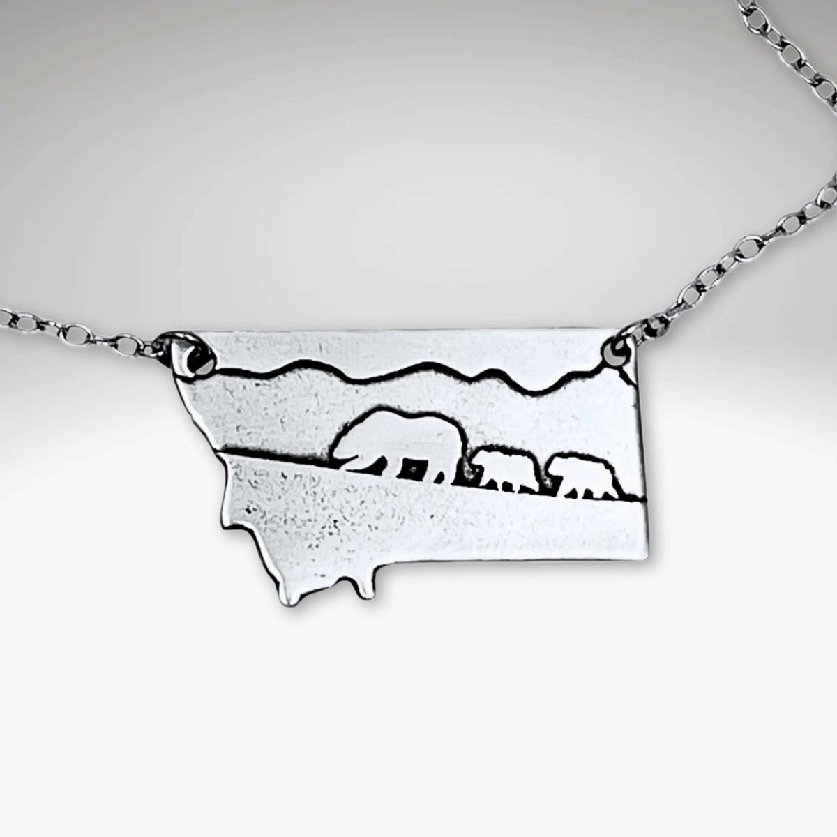 Mama and Cubs Necklace featuring an etched design of a grizzly bear and her cubs against a Montana backdrop.