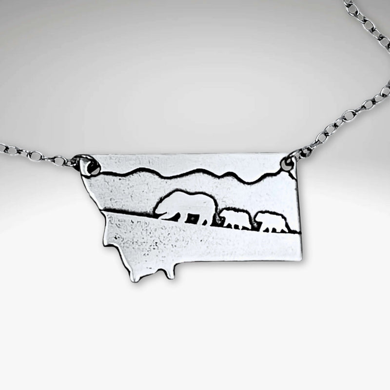 Mama and Cubs Necklace featuring an etched design of a grizzly bear and her cubs against a Montana backdrop.