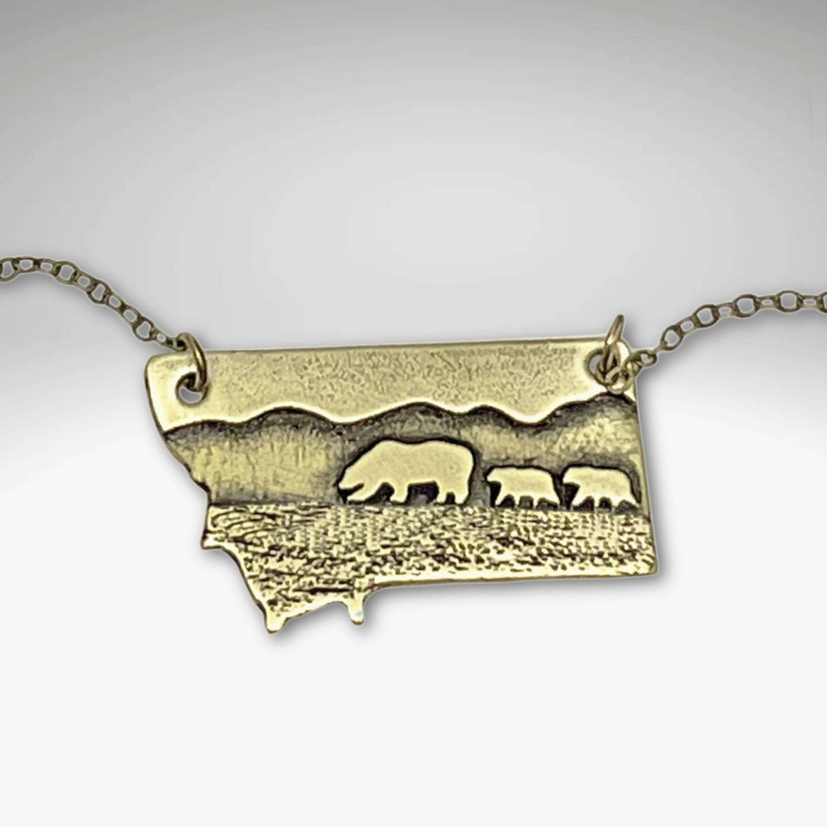 Mama and Cubs Necklace featuring a mother grizzly bear and cubs on a Montana-inspired raw brass pendant.