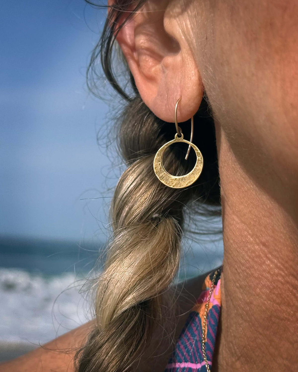 Model wearing Mini Discs Earrings in Antique Brass, showcasing their handmade texture by the beach.