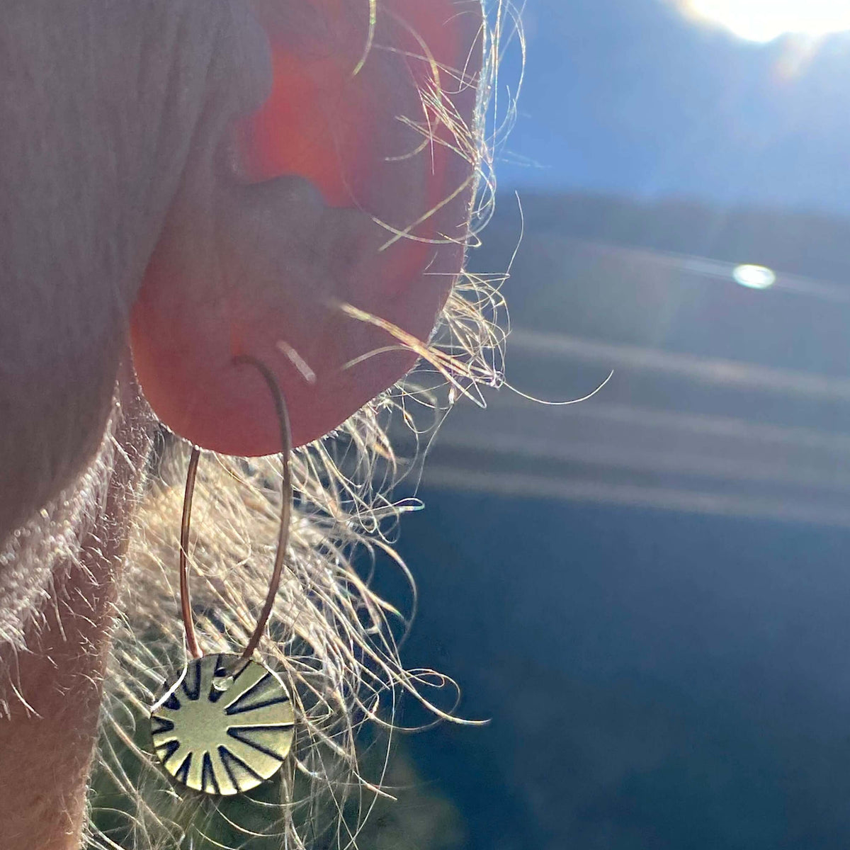 Close-up of Mini Sun Ray Hoop Earrings worn, showcasing stylish sun rays design against a bright background.