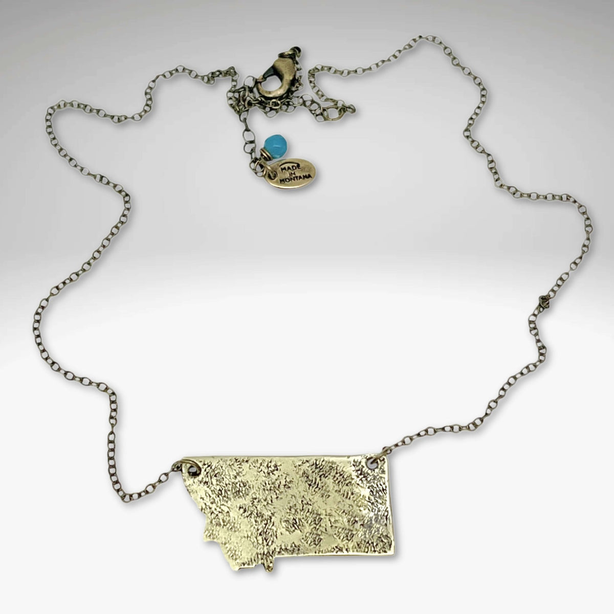 Montana Necklace on a light cable chain with textured Montana outline and charm, adjustable length up to 30 inches.