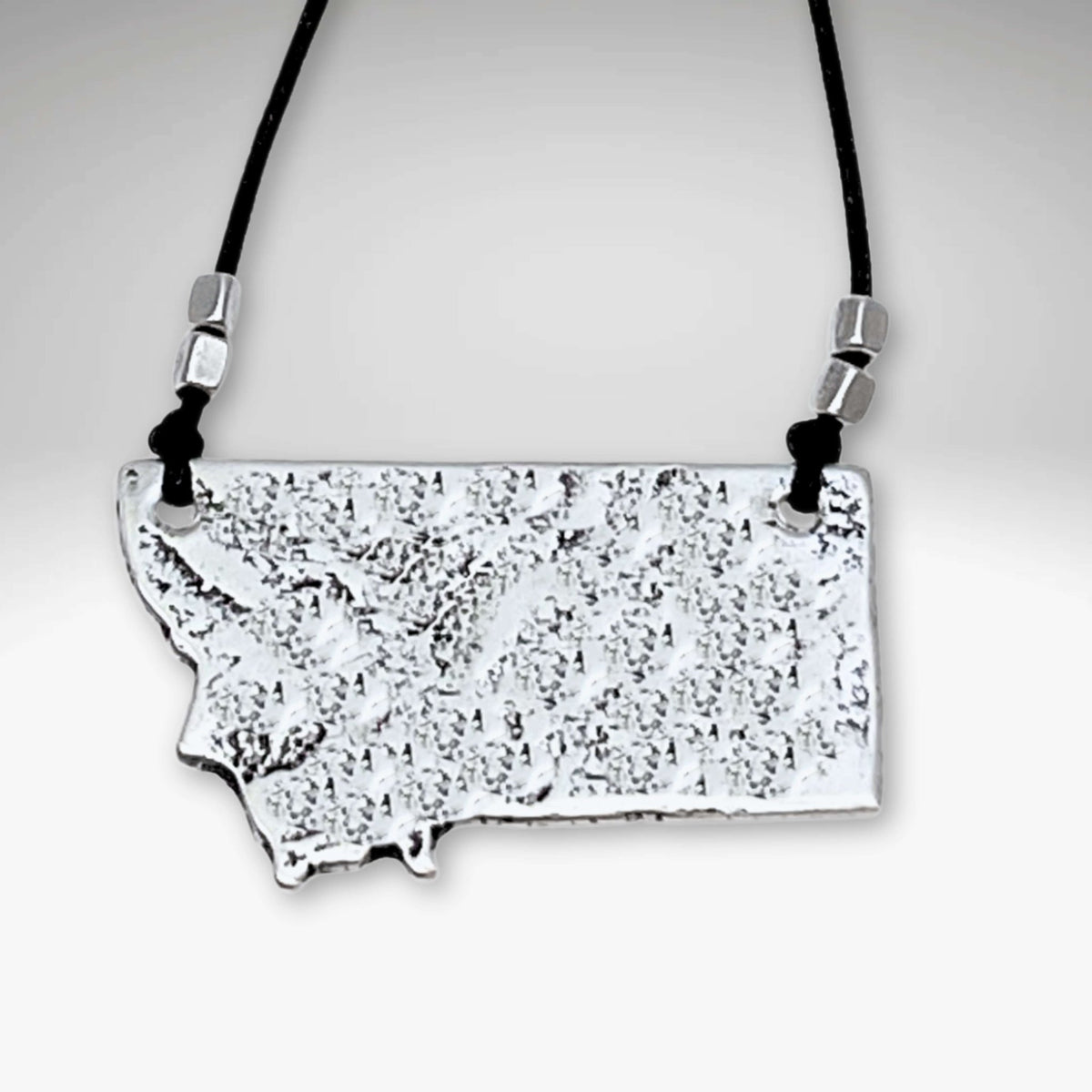 Montana Necklace featuring a textured outline of Montana on a black cord, representing home and earthiness.