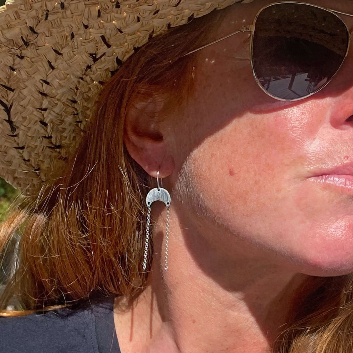 Woman wearing Moonfall Earrings with a silver finish, set against a sunny outdoor background.
