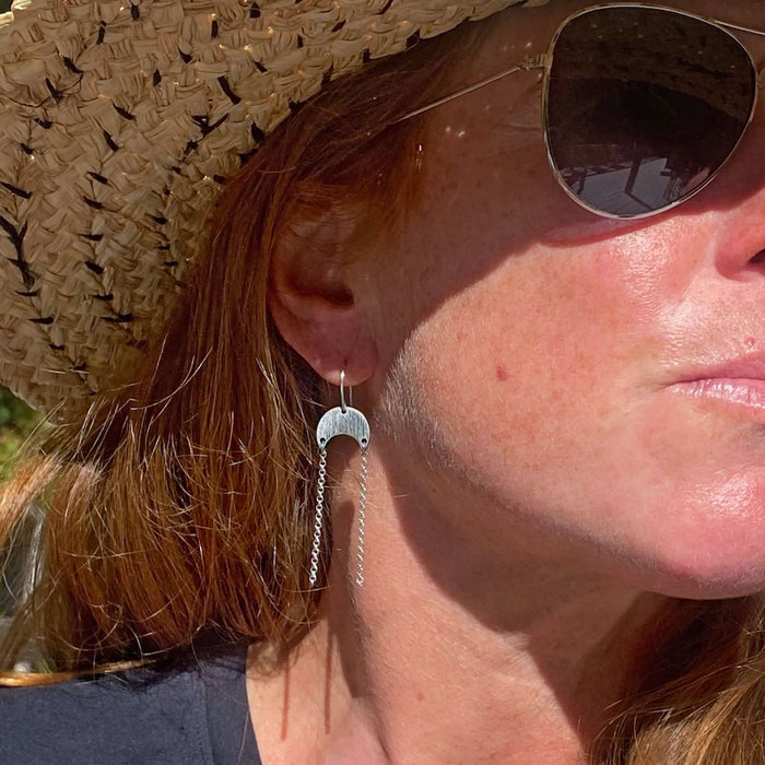 Woman wearing Moonfall Earrings with a silver finish, set against a sunny outdoor background.