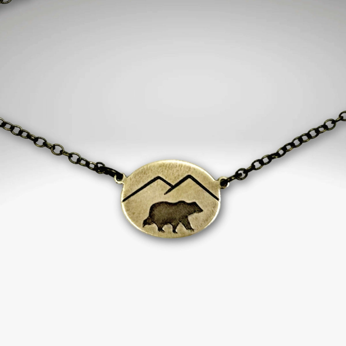 Mountain Bear Necklace showcasing antique brass finish with bear and mountain design on a black chain.
