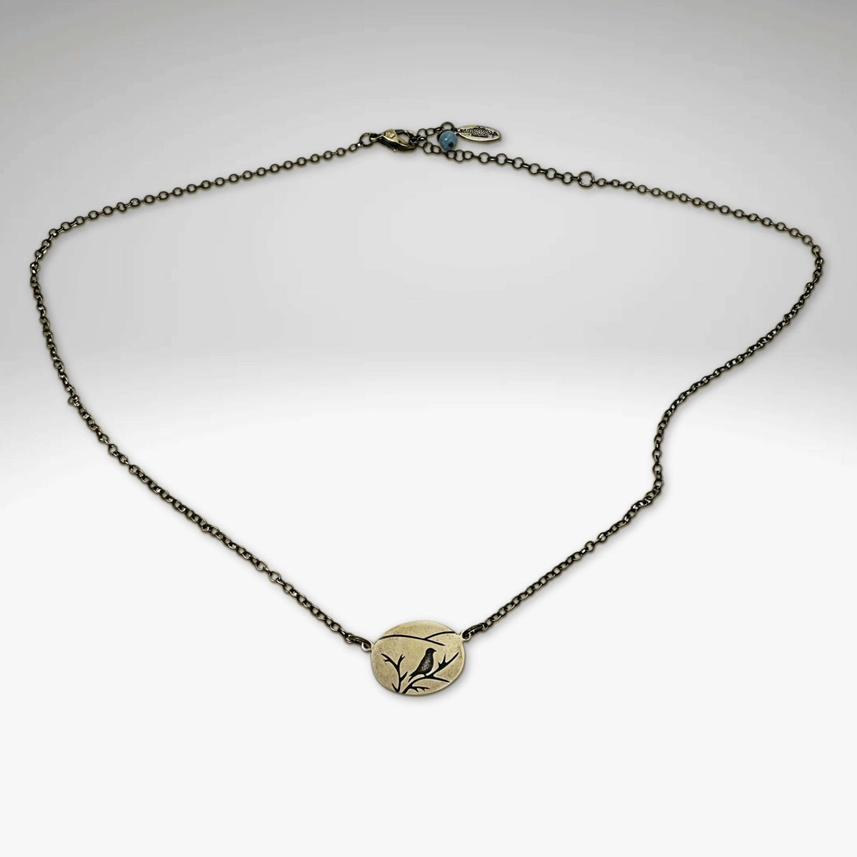 Mountain Bluebird Necklace featuring a delicate bluebird and mountain on an oval pendant, adjustable from 16-18 inches.