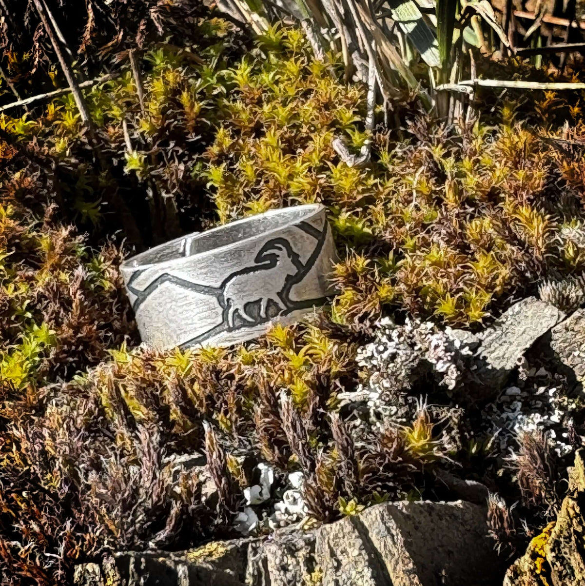 Mountain Goat Adjustable Ring displayed on a bed of moss and rocks, showcasing its unique design and natural elements.