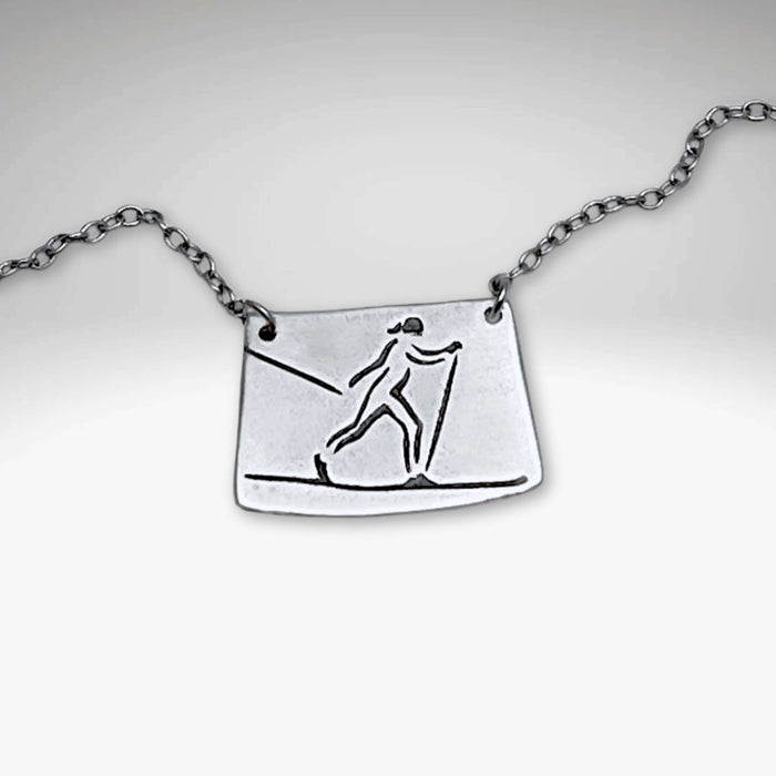 Nordic Run Necklace featuring a unique etching of a skier on a simple cable chain, perfect for winter travel lovers.