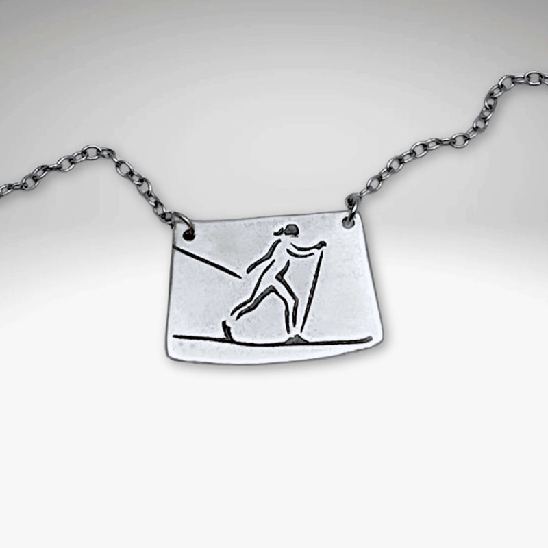 Nordic Run Necklace featuring a unique etching of a skier on a simple cable chain, perfect for winter travel lovers.