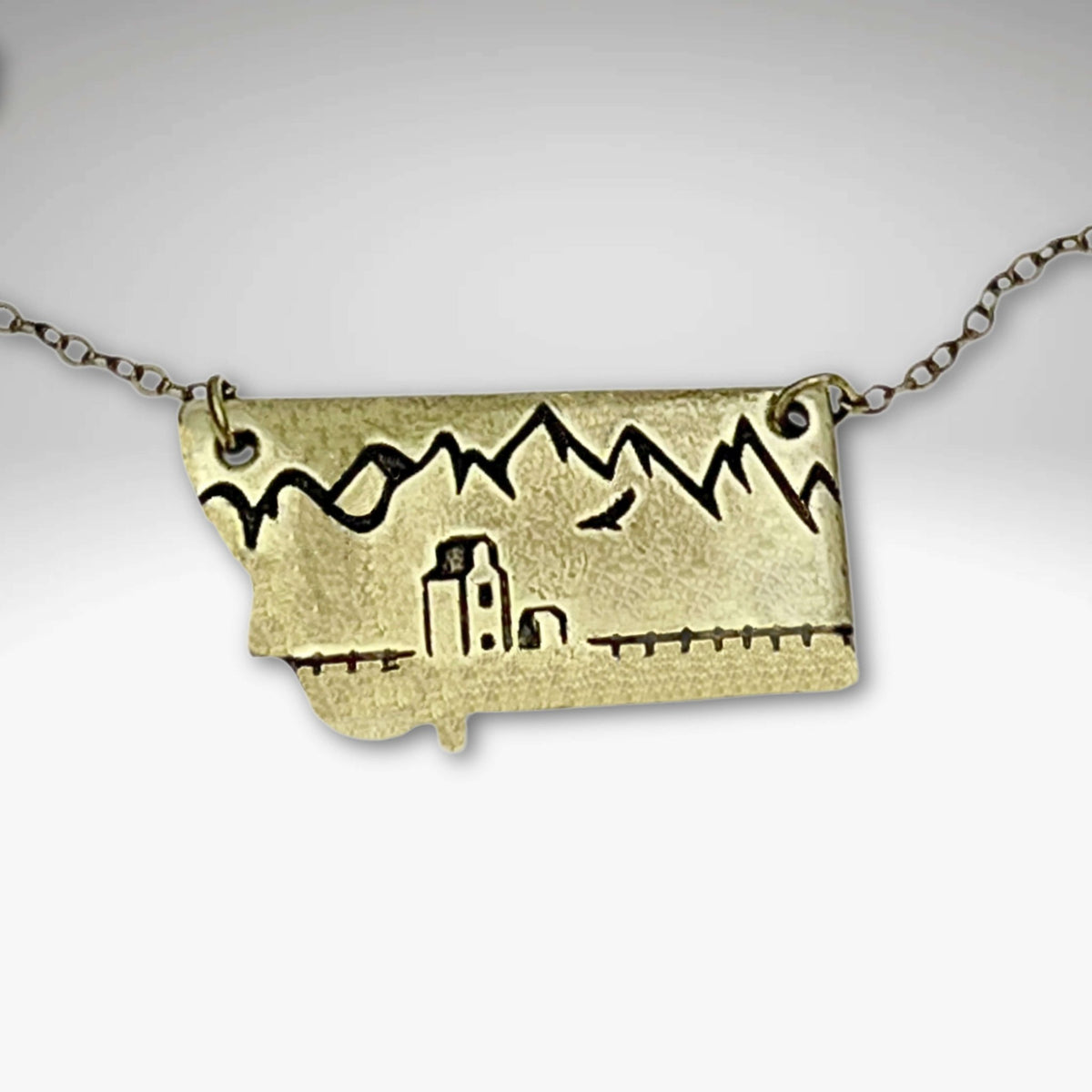 On the Front in Montana Necklace featuring a grain elevator and mountains carved on raw brass.