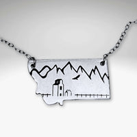 On the Front in Montana Necklace featuring a grain elevator and mountains, crafted in raw brass with adjustable chain.