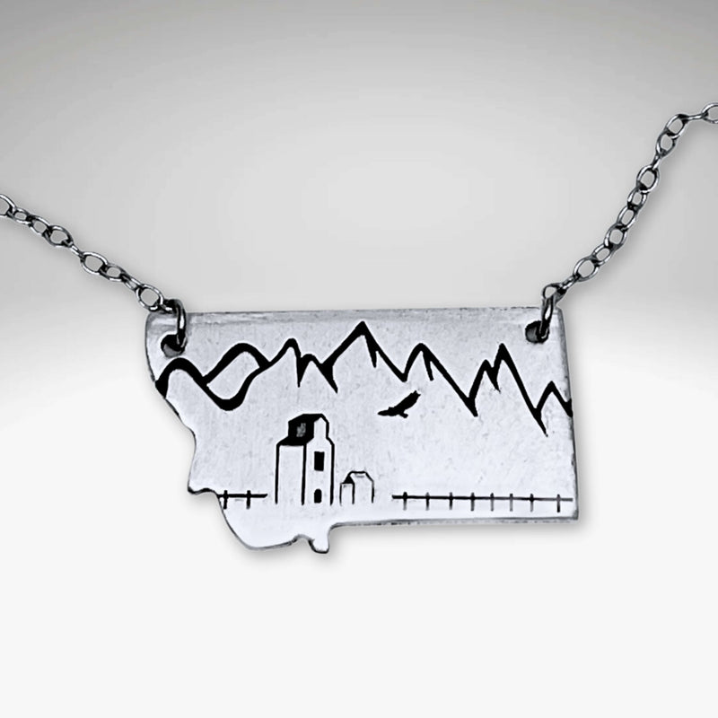 On the Front in Montana Necklace featuring a grain elevator and mountains, crafted in raw brass with adjustable chain.
