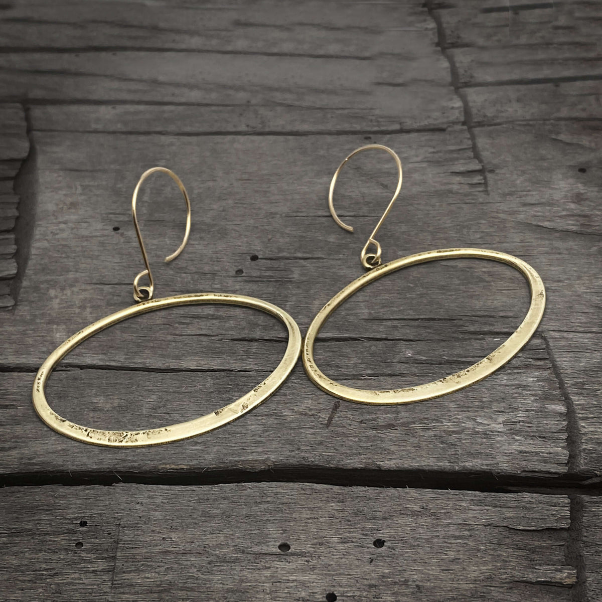 Open Space Earrings featuring hammered gold ellipses on a rustic wooden background.