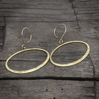 Open Space Earrings featuring hammered gold ellipses on a rustic wooden background.