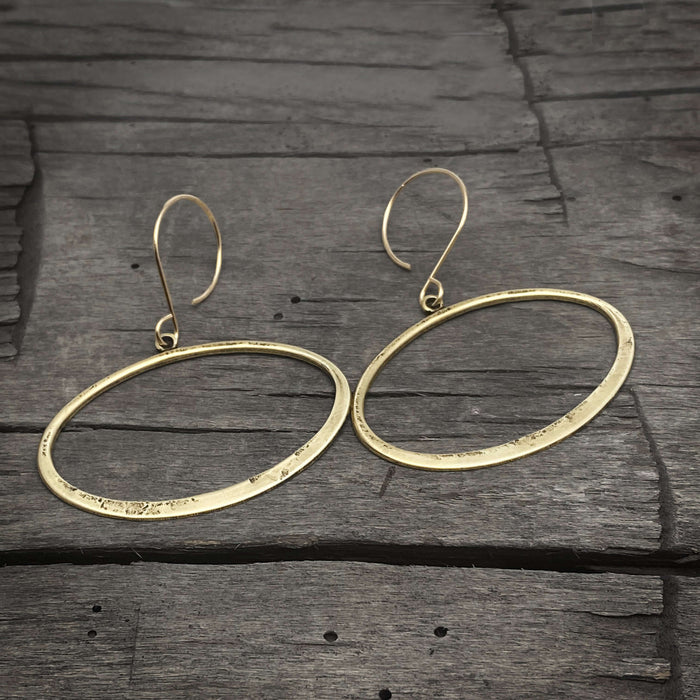 Open Space Earrings featuring hammered gold ellipses on a rustic wooden background.