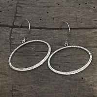 Open Space Earrings featuring lightly hammered silver open ellipses on a wooden surface.