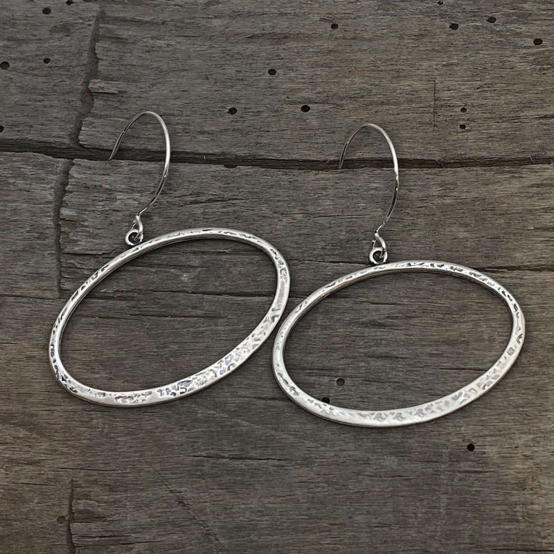 Open Space Earrings featuring lightly hammered silver open ellipses on a wooden surface.