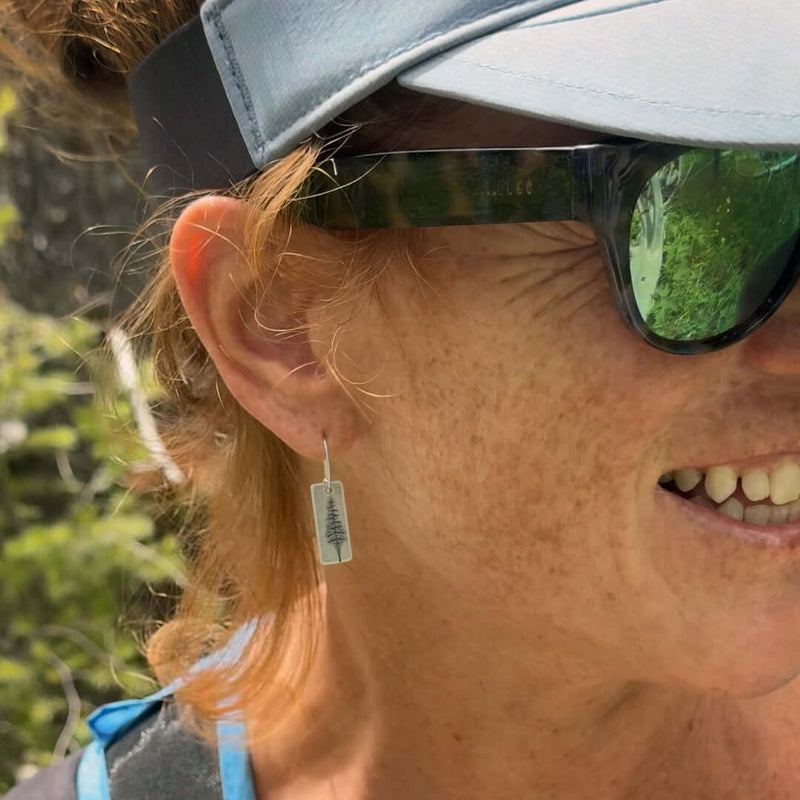 Woman wearing P Pine Tree Earrings while outdoors, showcasing their contemporary design and nature-inspired style.