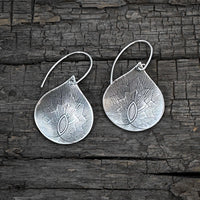Petals Earrings in matte silver finish, featuring floral-inspired teardrop design against a rustic wooden background.