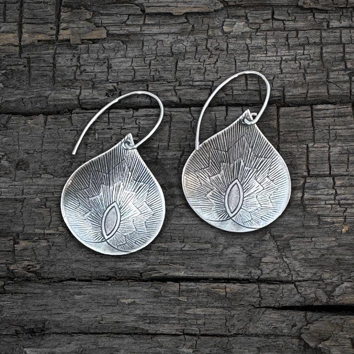 Petals Earrings in matte silver finish, featuring floral-inspired teardrop design against a rustic wooden background.
