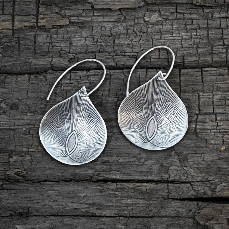Petals Earrings in matte silver finish, featuring floral-inspired teardrop design against a rustic wooden background.