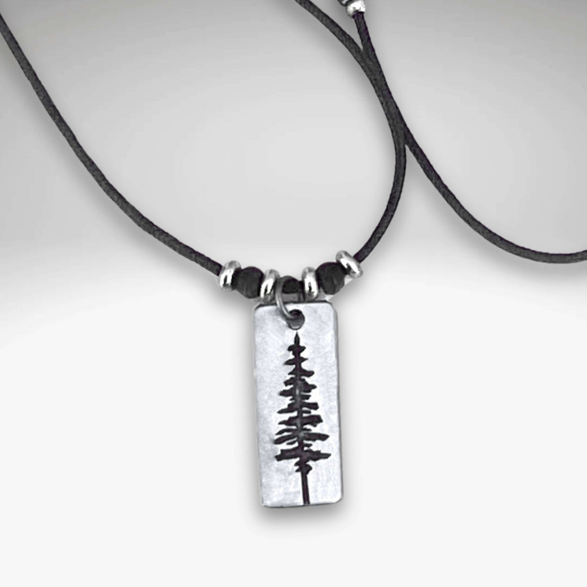 Elegant Pine Tree Necklace with a silver pendant on a leather cord, perfect for nature lovers.