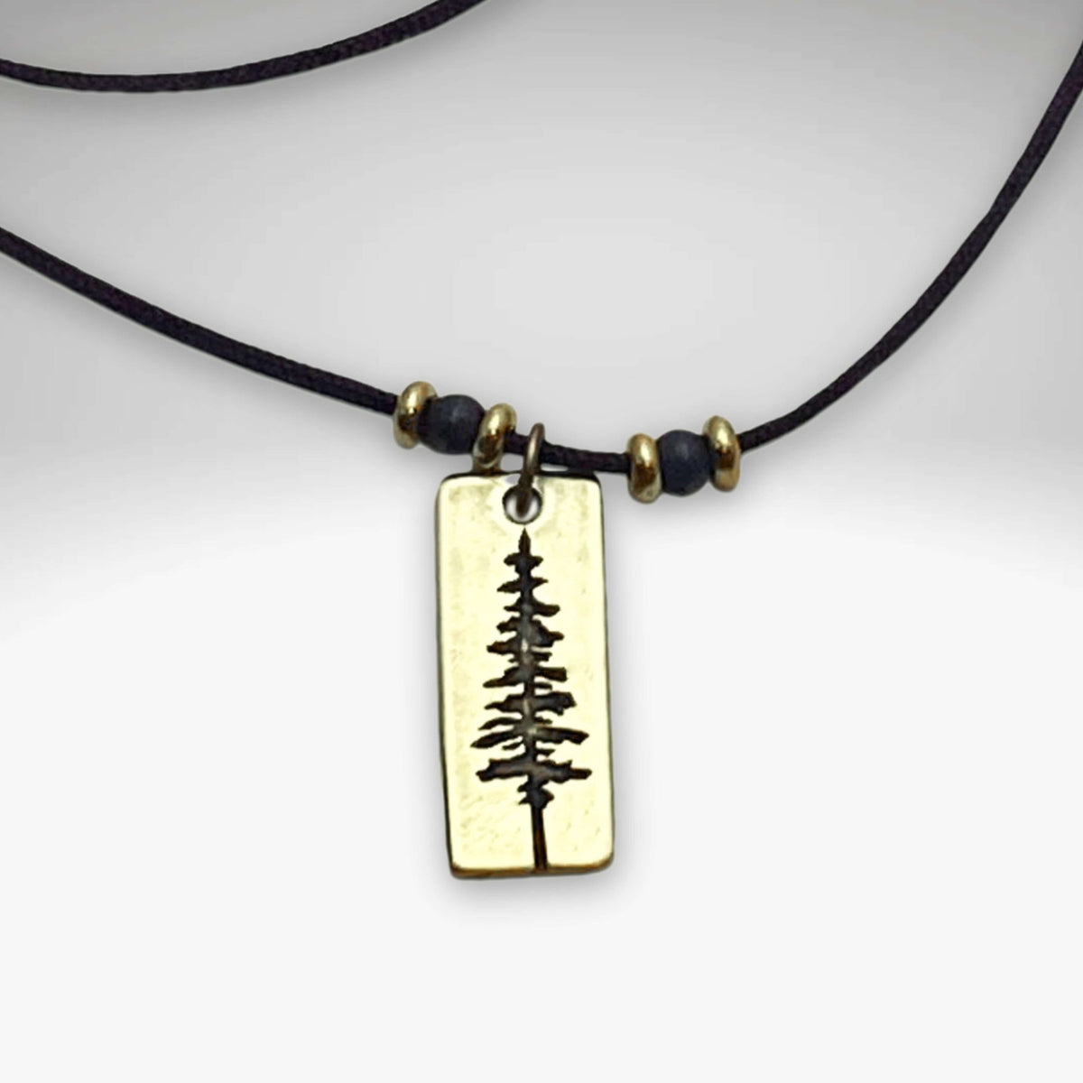 Pine Tree Necklace featuring a Ponderosa Pine pendant on a black cord with beads, available in antique brass finish.