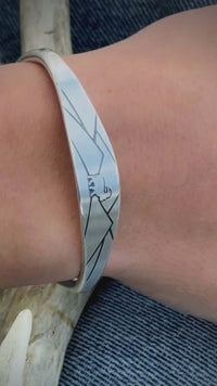 Handcrafted mountain goat cuff bracelet in matte silver, displayed on a wrist against denim and antler.