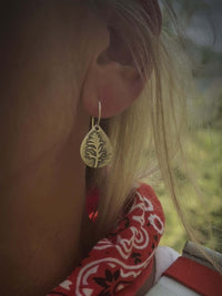 Teardrop earrings featuring a vibrant wildflower design in antique brass, worn by a person outdoors.