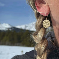 Close-up of Going to the Sun Earrings worn outdoors, showcasing a nature-inspired design against a mountain backdrop.