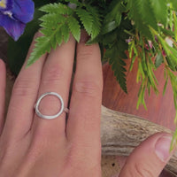 Person wearing a Halo Adjustable Ring, featuring a simple open circle, surrounded by green foliage and flowers.