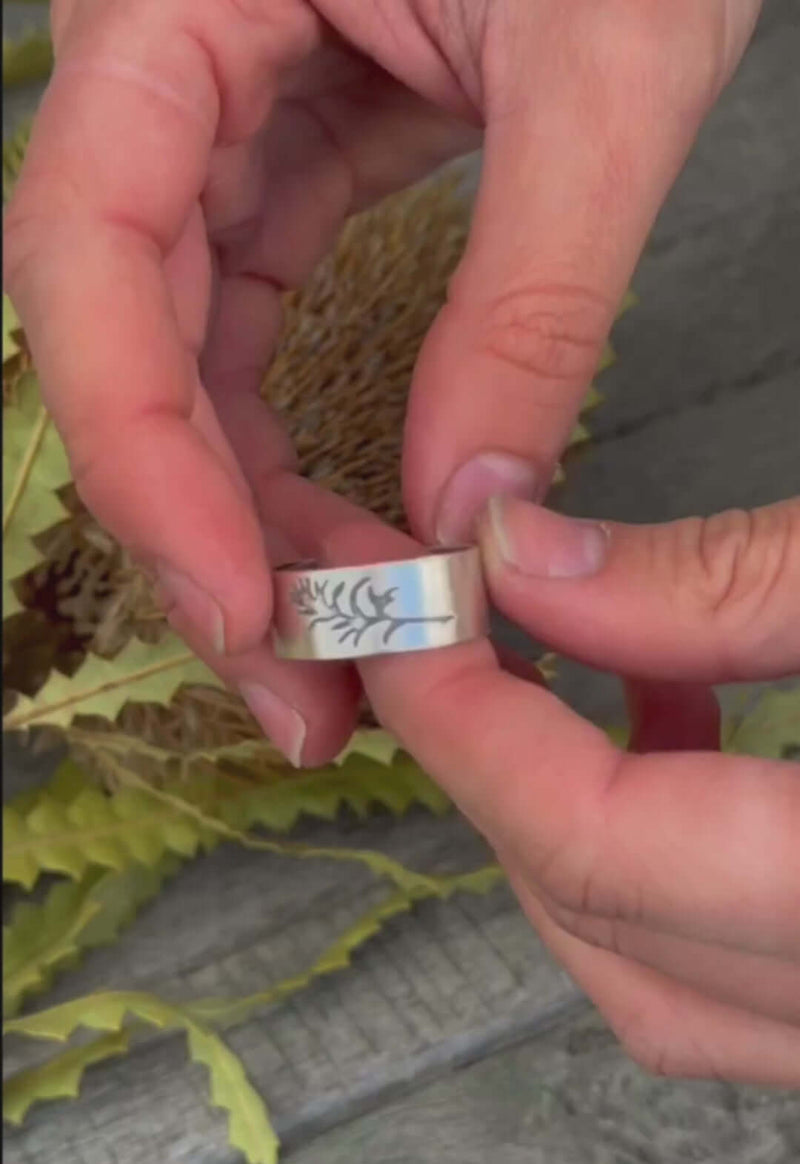 Close-up of hands holding a Paintbrush Adjustable Ring showcasing a wildflower design against a natural background.