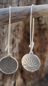 simple pair of round disc earrings with sunrise design matte silver hanging from a stick