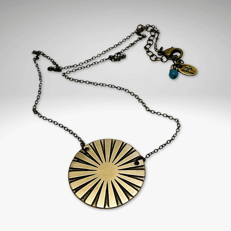 Ray Necklace featuring a sunray disk design in Antique Brass, adjustable chain or monofilament cord options.