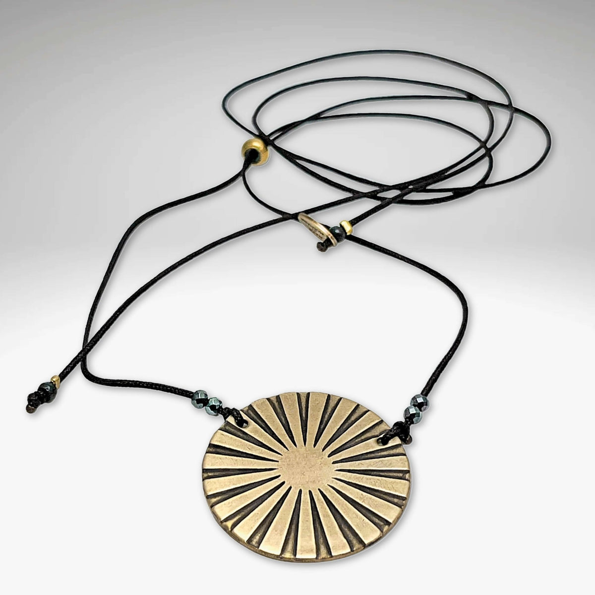 Ray Necklace featuring a sun ray disk in antique brass with a lightweight adjustable cord.