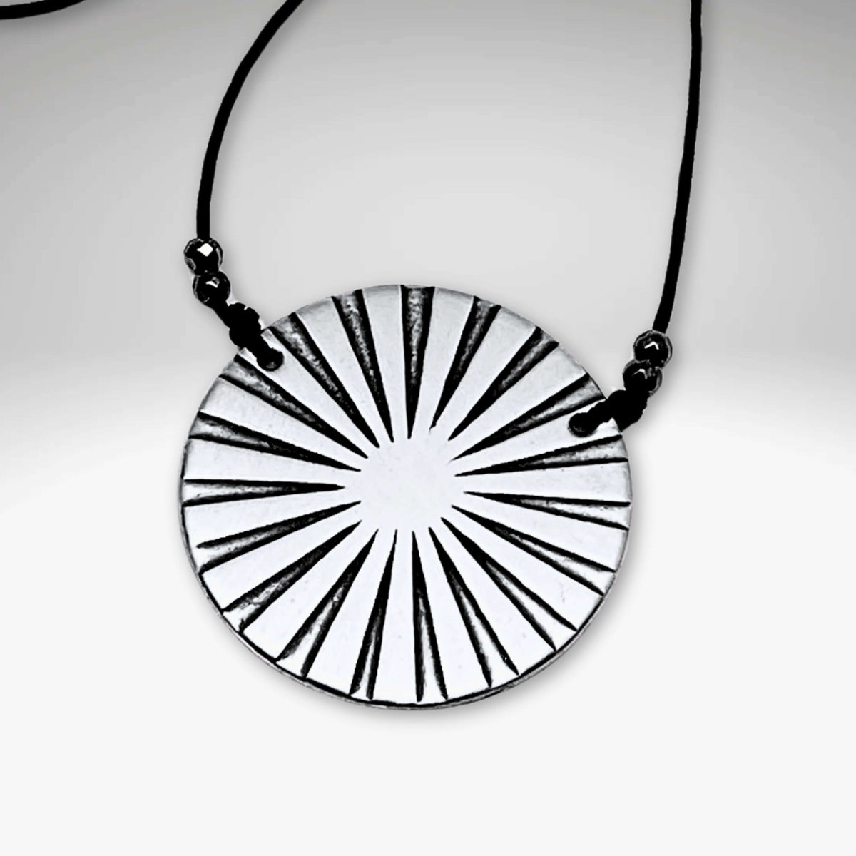 Ray Necklace featuring a sunburst disk pendant on a cable chain, available in Matte Silver and Antique Brass finishes.