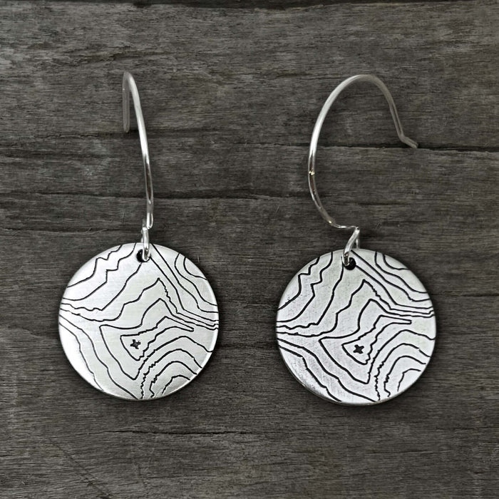 Rising Wolf Earrings featuring topographic design of Rising Wolf Mountain in silver finish against rustic wood background.