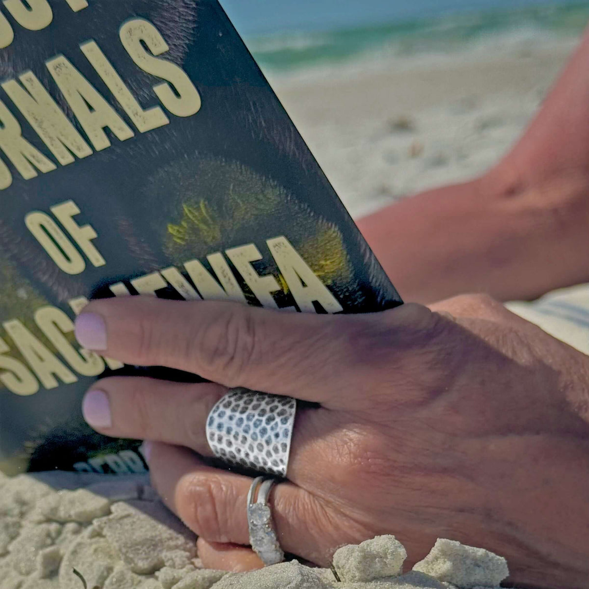 Person wearing a Rubble Adjustable Ring while reading a book on the beach.