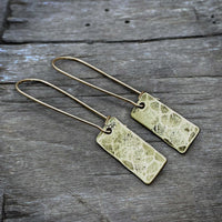 Rubble Rectangles Earrings featuring hand-hammered brass rectangles with antique finish on a wooden background.