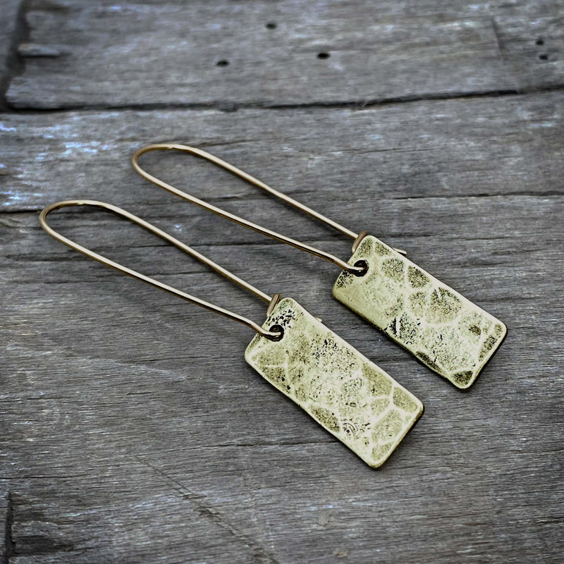 Rubble Rectangles Earrings featuring hand-hammered brass rectangles with antique finish on a wooden background.
